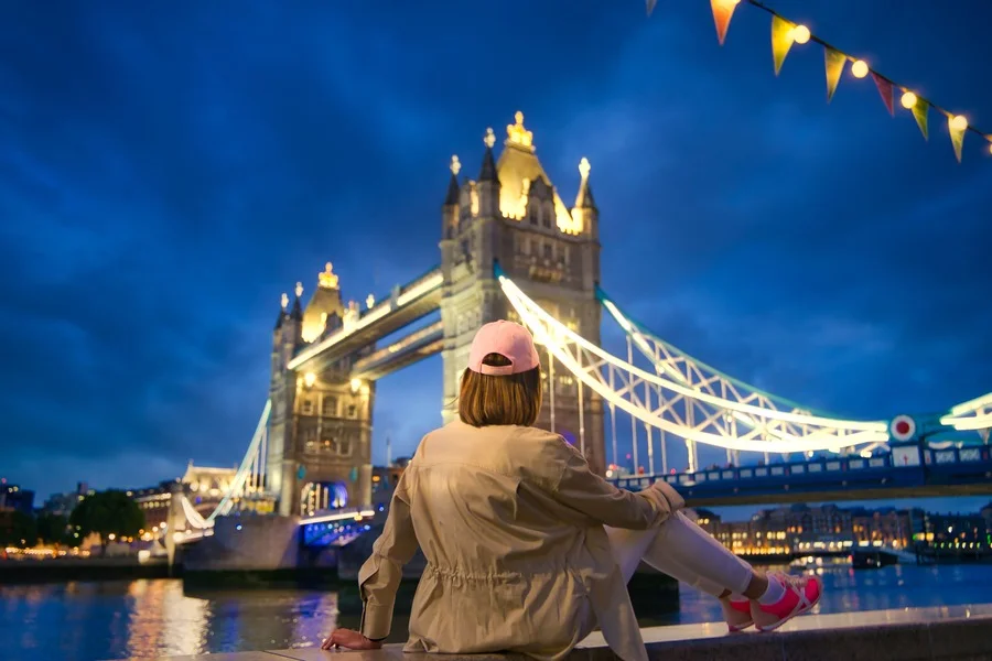 Woman sitting by the River Thames with Tower Bridge in the background at night, London