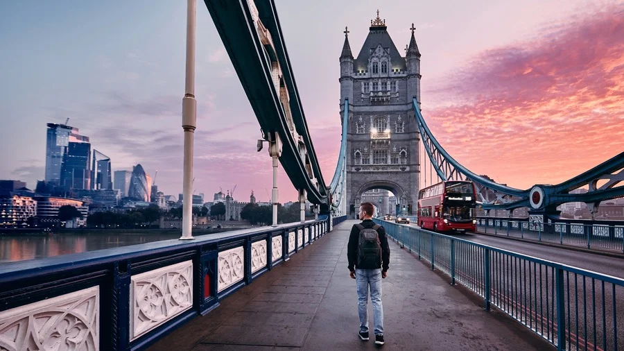Man with backpack standing on Tower Bridge at sunset in London