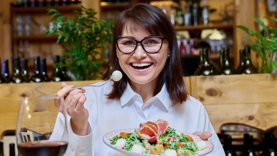 Middle-aged Italian woman joyfully eating salad in a Rome restaurant
