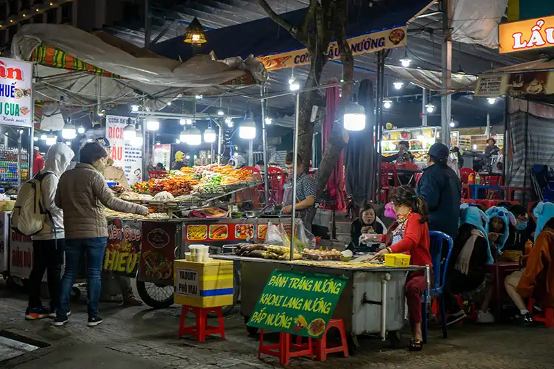 Street food carts selling Vietnamese snacks and barbecue at Dalat Night Market, City Center, Da Lat, Vietnam.