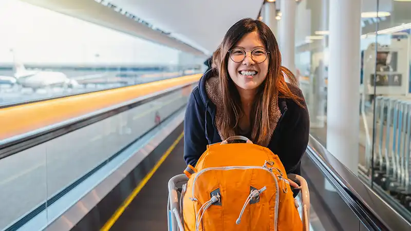 Asian tourist excitedly arriving at airport, smiling and walking on escalator.