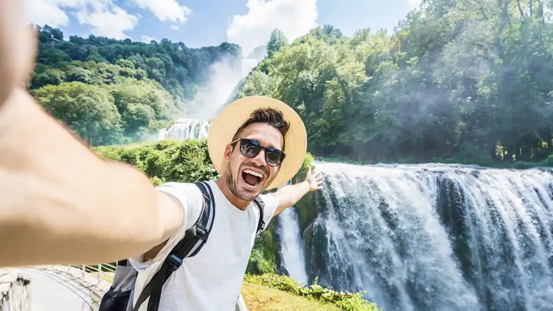 Tourist taking a selfie in front of a majestic waterfall.