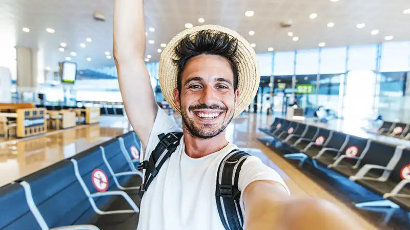 Happy tourist man taking a selfie at airport with a smartphone.
