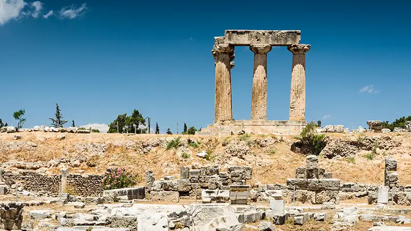 Ruins of the ancient Temple of Apollo in Corinth, Greece, against a clear sky.