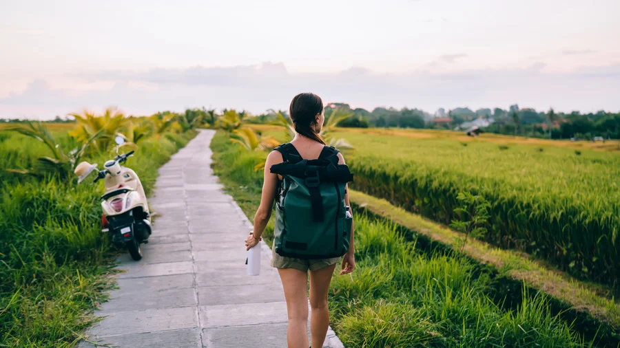 Woman with backpack walking on a path beside rice fields in Bali, Indonesia, for Bali travel guide.