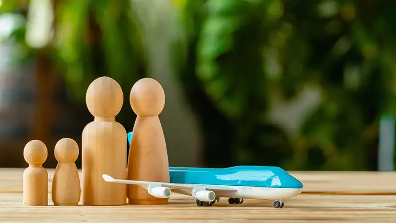 Wooden figures representing a family next to a toy plane, symbolizing family travel and the consideration of whether travel insurance is necessary.