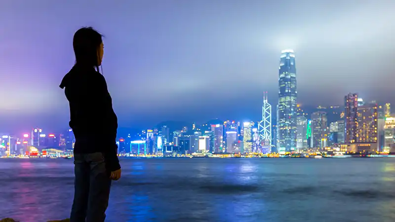 Girl marveling at the Hong Kong skyline at night, a must-do experience in Hong Kong.