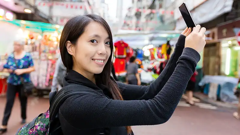 Woman taking a selfie at the vibrant Temple Street in Hong Kong, a must-visit destination.