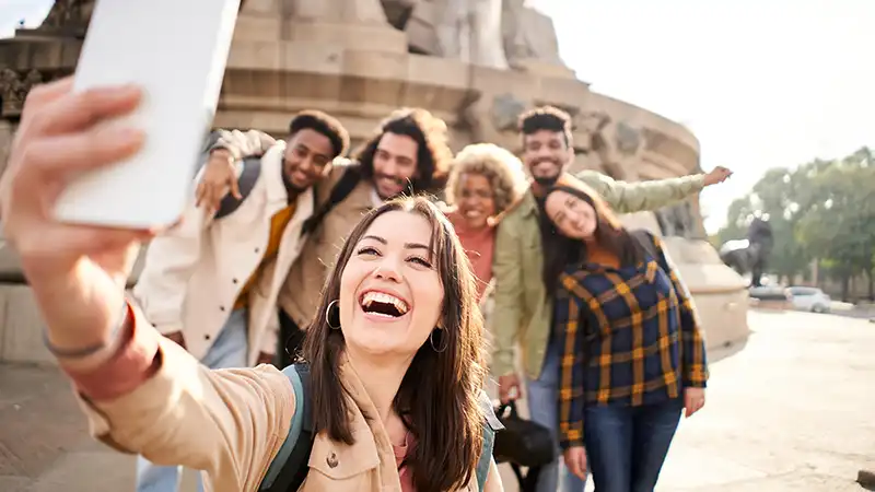 Cheerful group of college students taking a selfie on campus, a reminder of the joys of student travel and the importance of considering if travel insurance is necessary.
