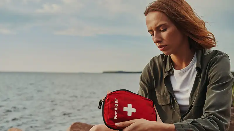 Traveler with first-aid kit in a scenic outdoor setting, symbolizing health preparedness in travel.